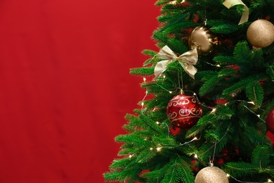 Beautiful Christmas tree with fairy lights and festive decor on red background