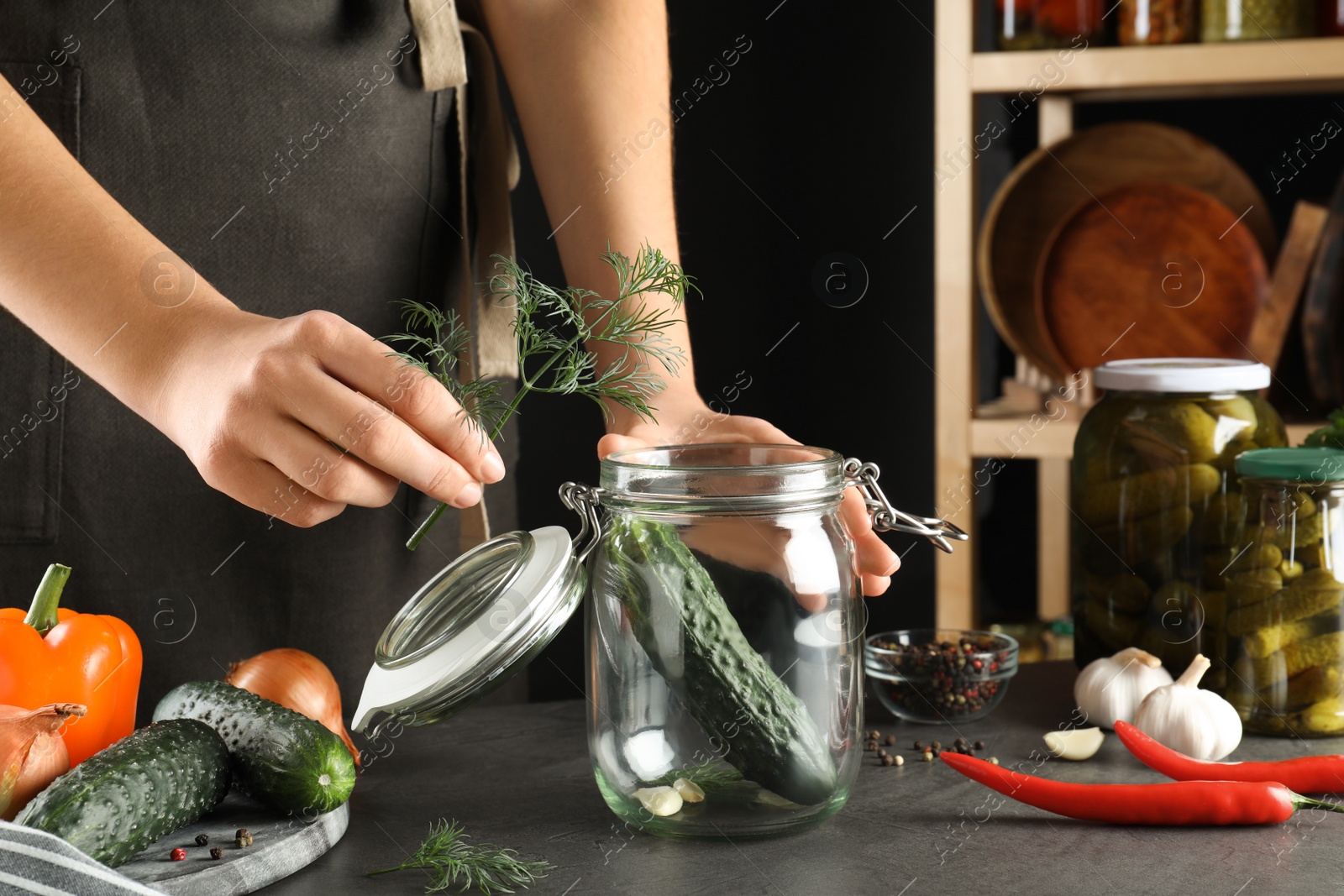 Photo of Woman putting dill into jar with cucumber at grey table, closeup