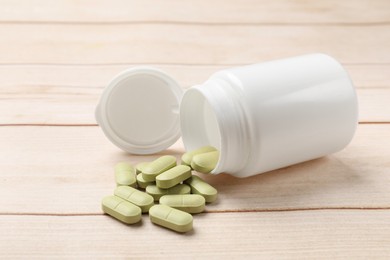 Photo of Bottle and vitamin pills on light wooden table