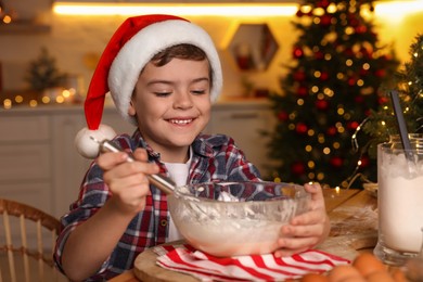 Photo of Cute little boy in Santa hat making dough for Christmas cookies at home