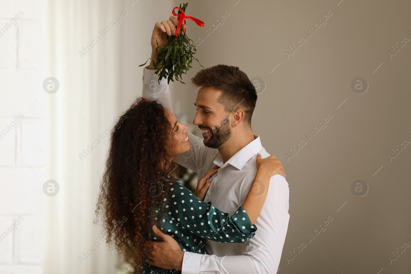 Photo of Lovely couple under mistletoe bunch in room. Christmas time