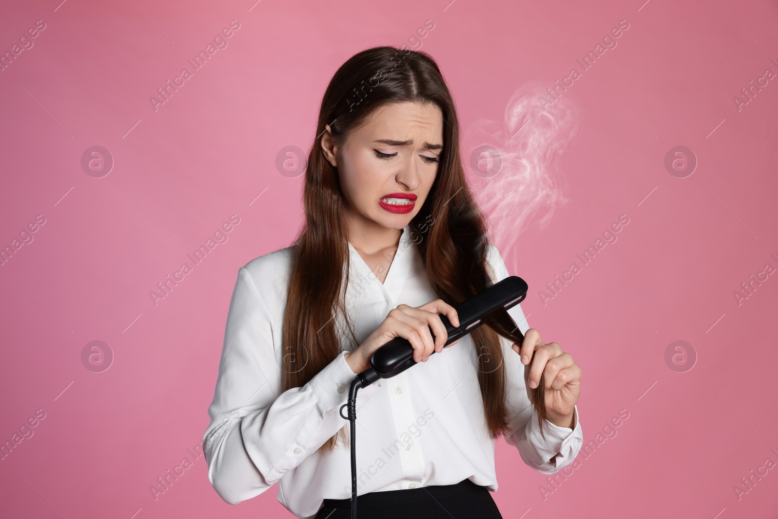 Photo of Upset young woman with flattening iron on light pink background. Hair damage