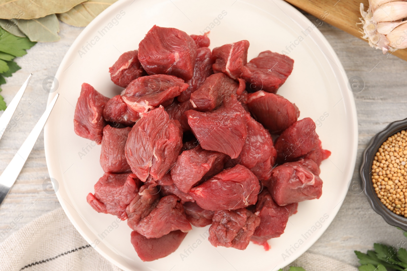 Photo of Plate with pieces of raw beef meat on light wooden table, top view