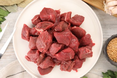 Photo of Plate with pieces of raw beef meat on light wooden table, top view