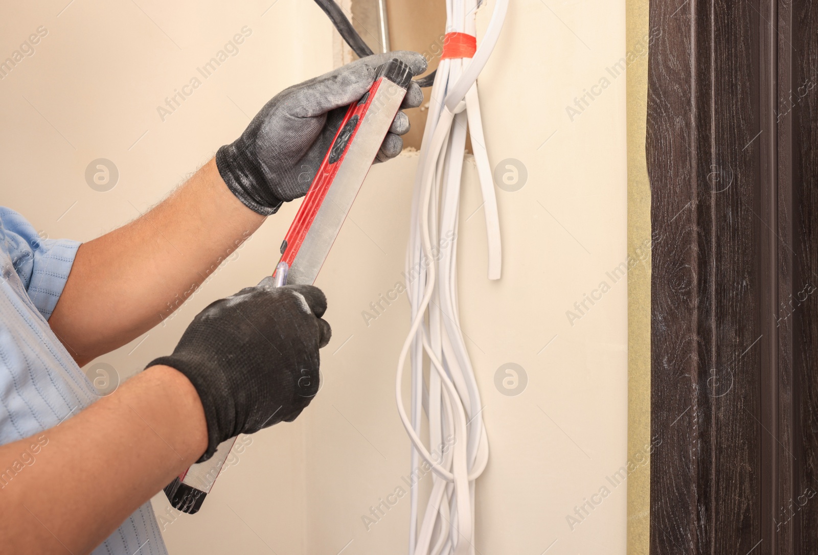 Photo of Electrician using spirit level indoors, closeup. Installation of electrical wiring