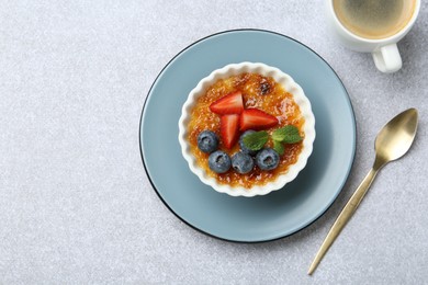 Delicious creme brulee with berries and mint in bowl served on grey textured table, flat lay. Space for text