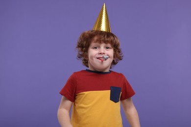 Photo of Cute little boy in party hat with blower on purple background