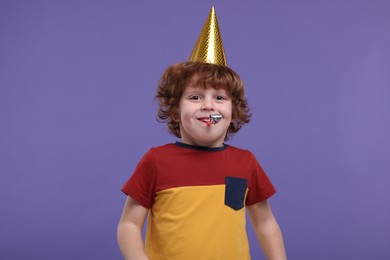 Cute little boy in party hat with blower on purple background