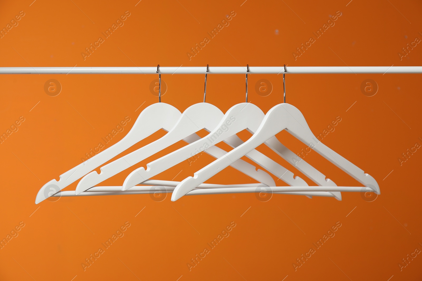 Photo of White clothes hangers on rack against orange background