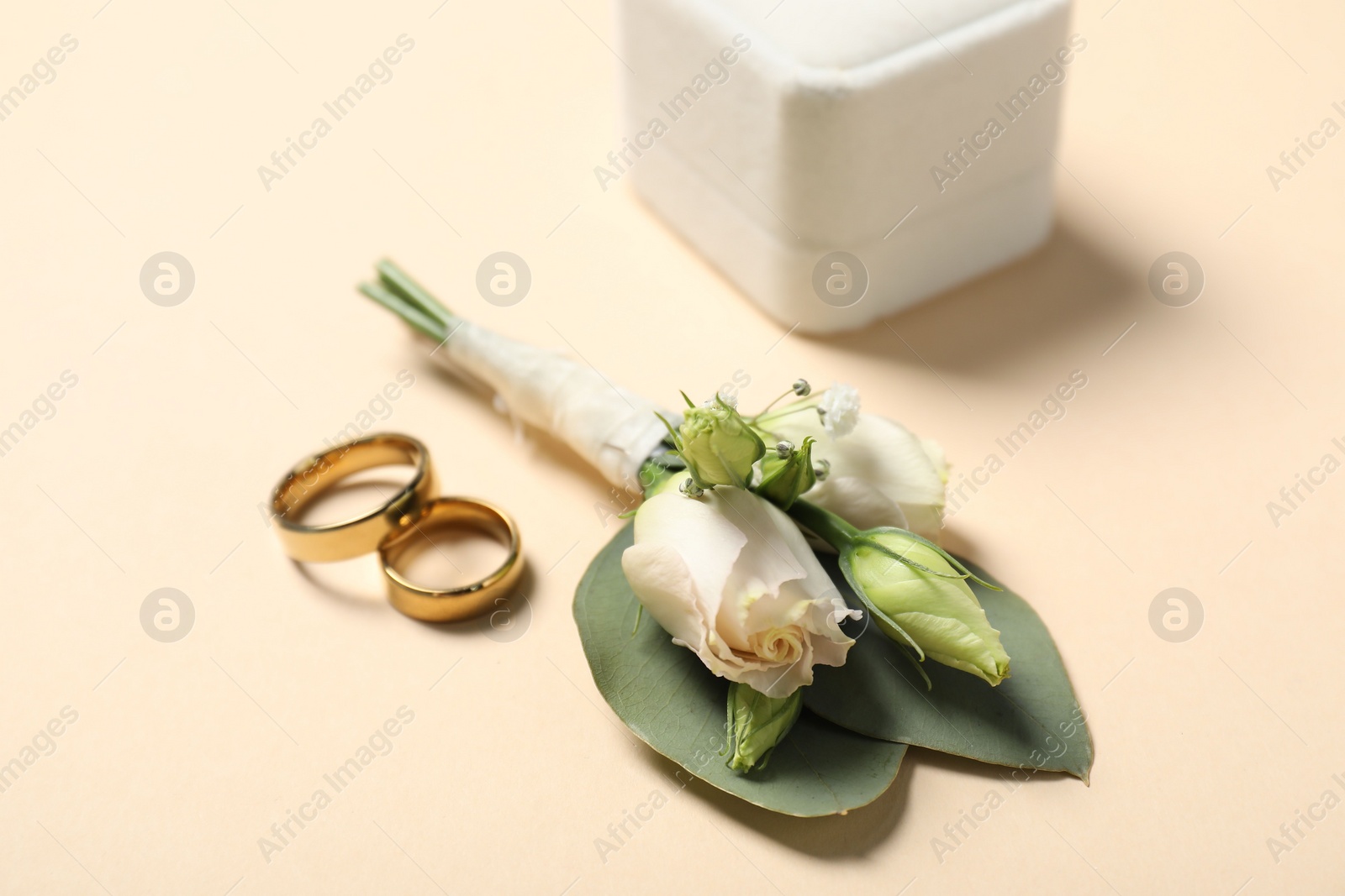 Photo of Wedding stuff. Stylish boutonniere and rings on beige background, closeup