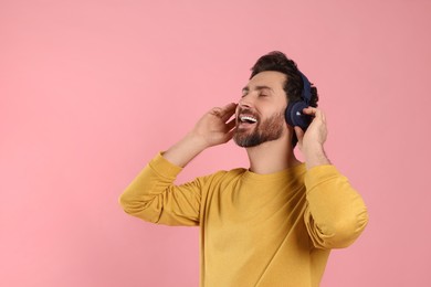 Photo of Happy man listening music with headphones on pink background. Space for text