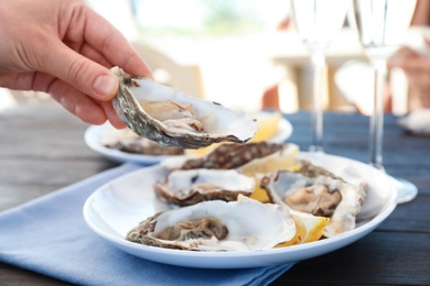 Photo of Woman with fresh oyster over plate, focus on hand