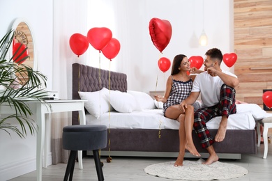 Photo of Young couple in bedroom decorated with air balloons. Celebration of Saint Valentine's Day