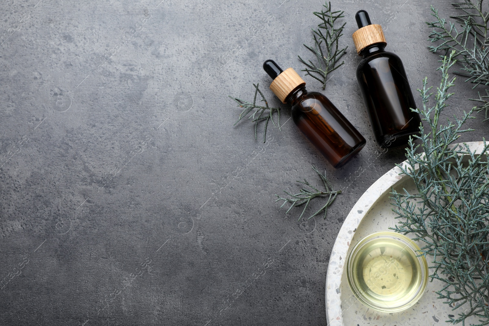 Photo of Juniper essential oil and fresh twigs on grey table, flat lay. Space for text