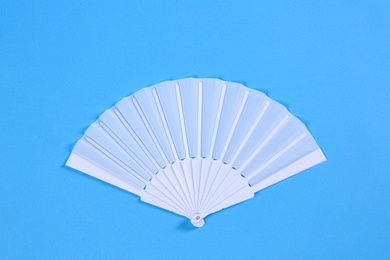 White hand fan on light blue background, top view