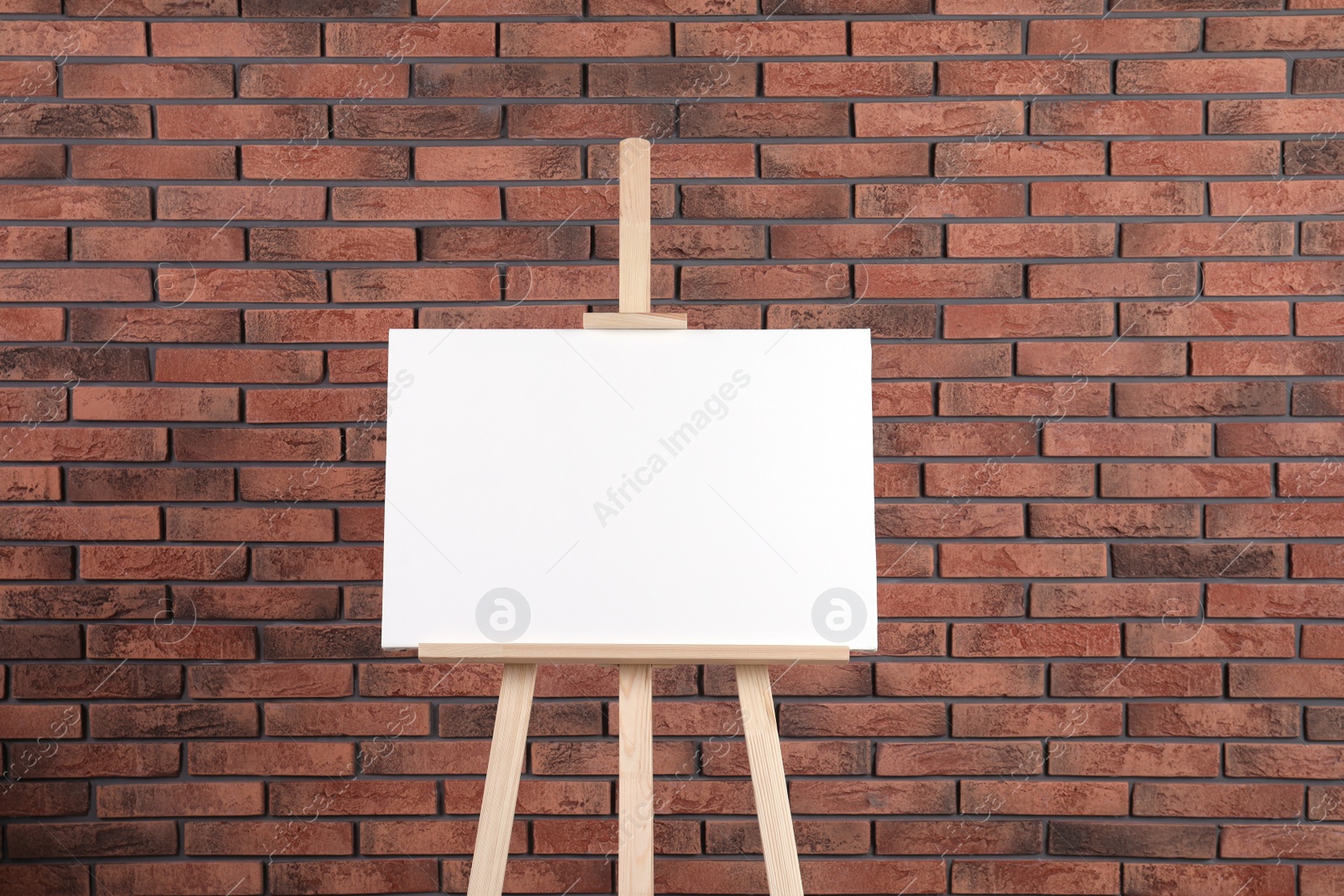 Photo of Wooden easel with blank canvas near brick wall