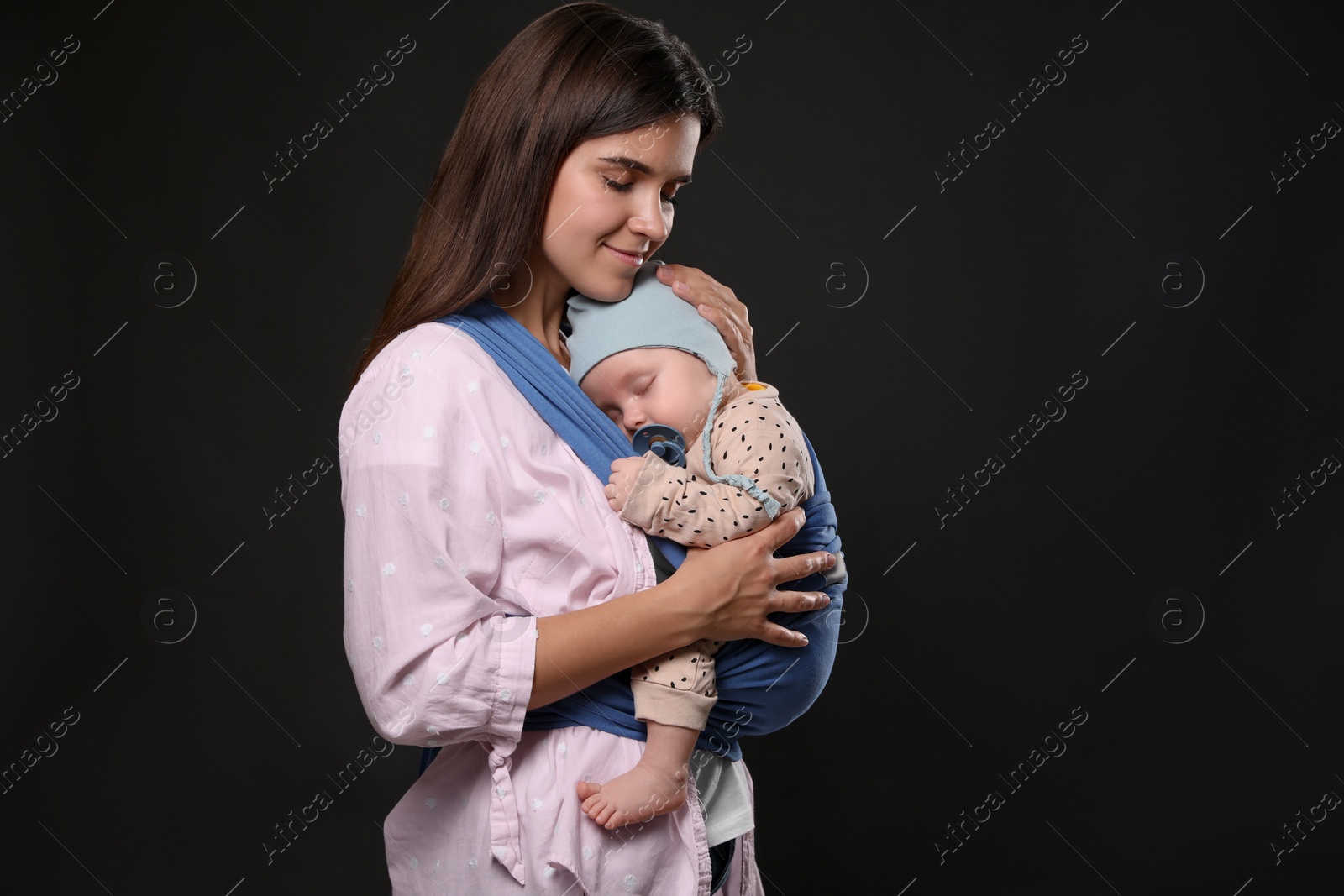 Photo of Mother holding her child in sling (baby carrier) on black background. Space for text