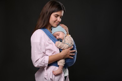 Photo of Mother holding her child in sling (baby carrier) on black background. Space for text