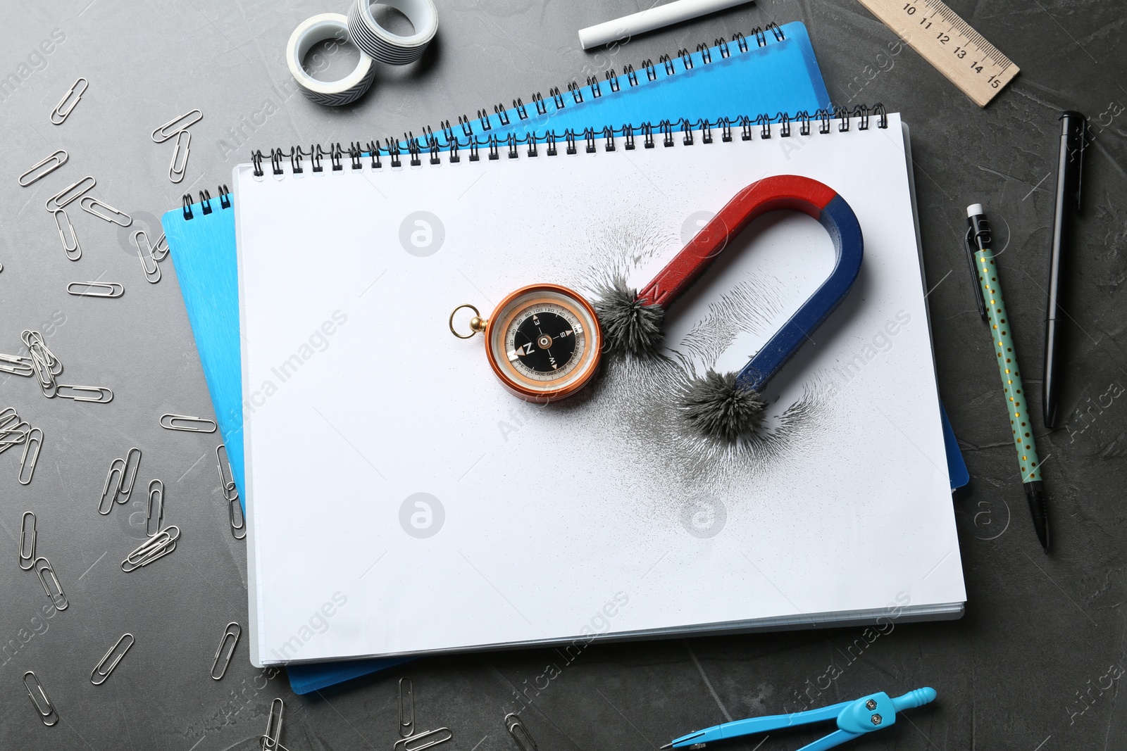 Photo of Notebooks, compass and magnet with iron powder on table, flat lay composition. Space for text