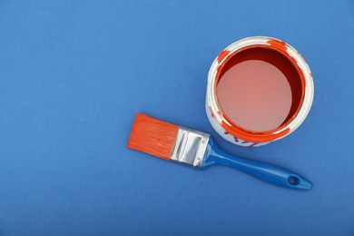 Photo of Can of orange paint and brush on blue background, top view. Space for text