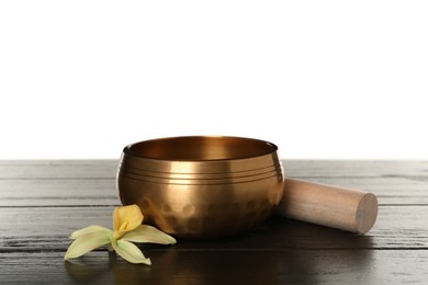 Golden singing bowl, mallet and flower on wooden table against white background