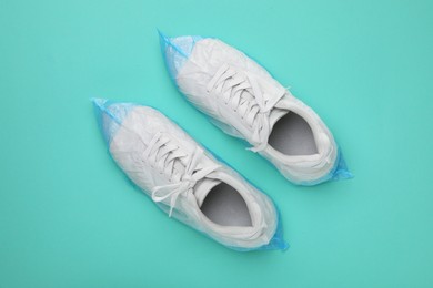 Photo of Sneakers in shoe covers on turquoise background, top view