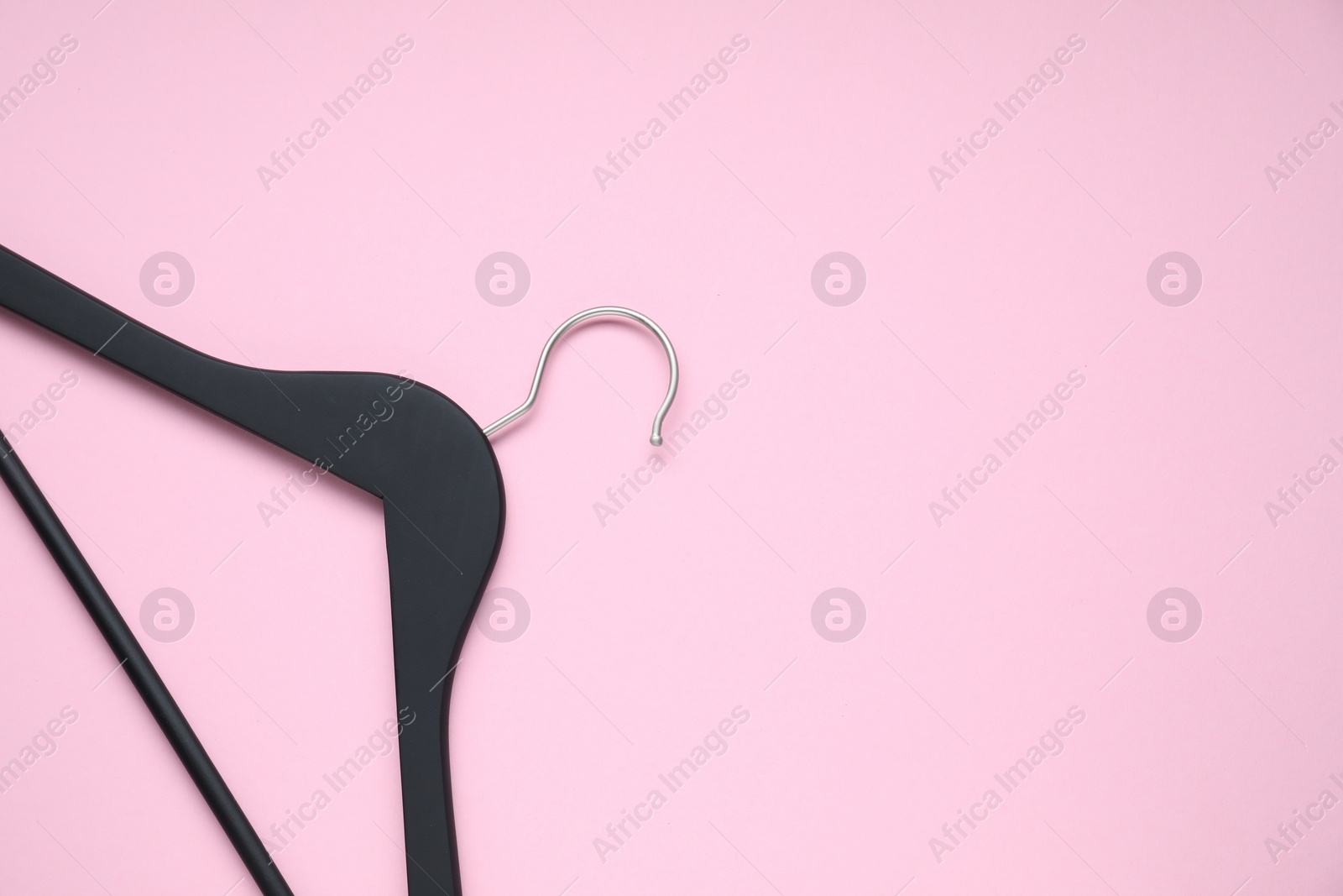 Photo of Empty black hanger on pink background, top view. Space for text