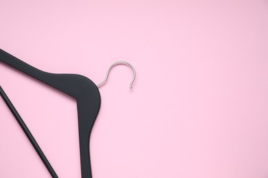 Empty black hanger on pink background, top view. Space for text