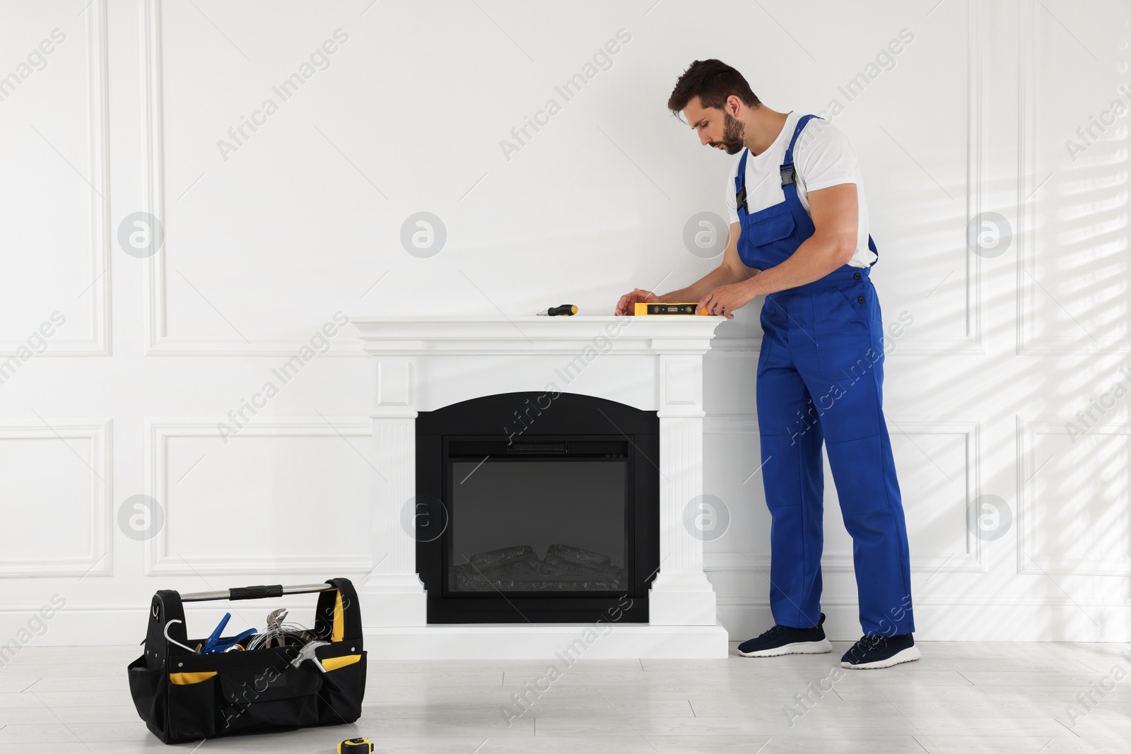 Photo of Professional technician using construction level for installing electric fireplace in room