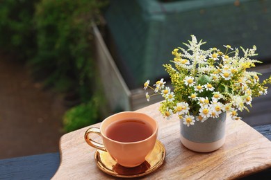 Photo of Cup of delicious chamomile tea and fresh flowers outdoors. Space for text