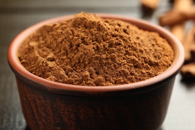 Bowl of cinnamon powder on wooden table, closeup