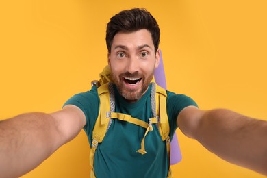 Photo of Happy man with backpack taking selfie on orange background. Active tourism