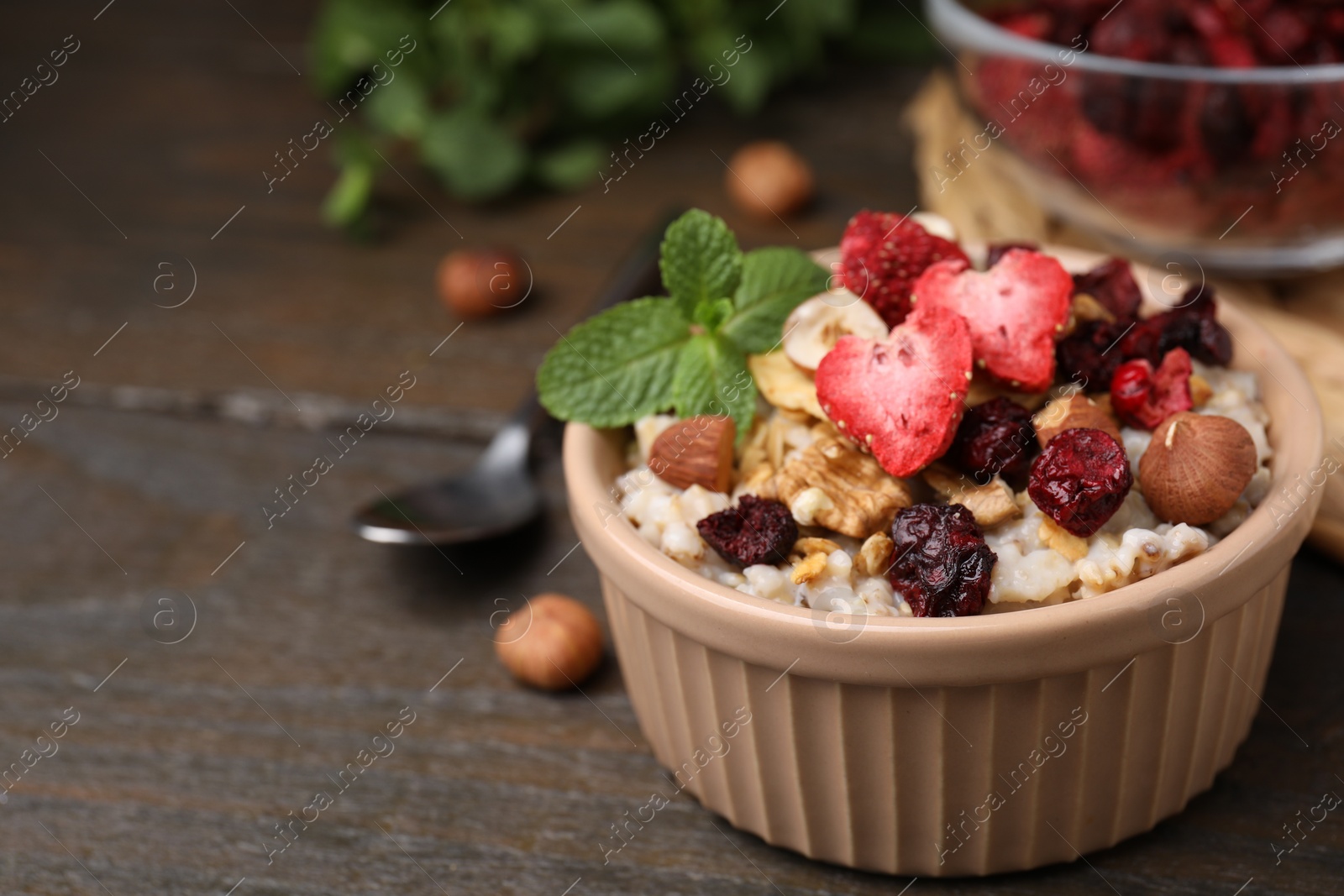 Photo of Oatmeal with freeze dried fruits, nuts and mint on wooden table, closeup. Space for text