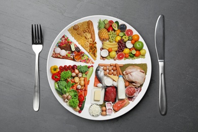 Image of Cutlery near plate with different products on grey table, flat lay. Balanced food