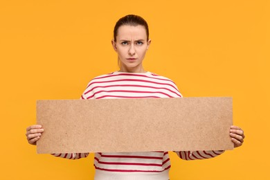Photo of Angry woman holding blank cardboard banner on orange background, space for text