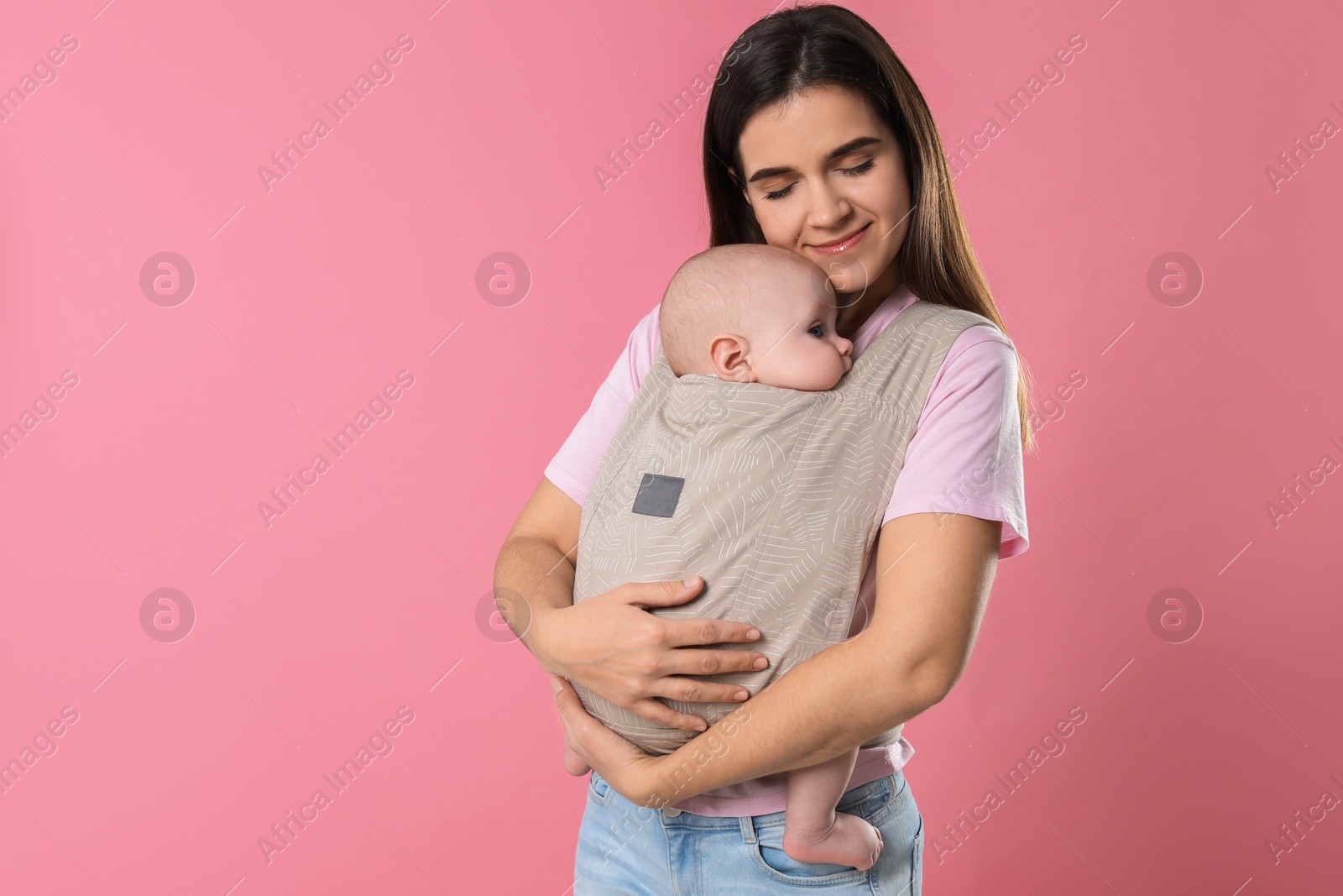 Photo of Mother holding her child in sling (baby carrier) on pink background. Space for text