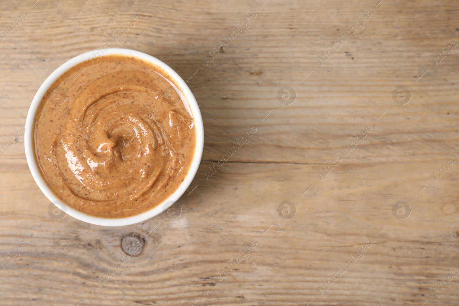 Photo of Delicious nut butter in bowl on wooden table, top view. Space for text