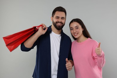 Happy couple with shopping bags showing thumbs up on grey background