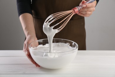 Woman making whipped cream with whisk at white wooden table, closeup