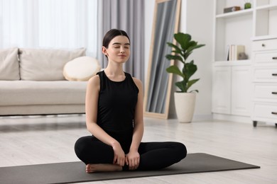 Beautiful girl meditating on yoga mat at home