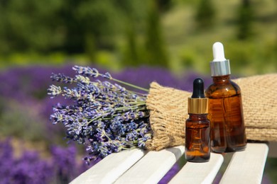 Photo of Bottles of essential oil and lavender flowers on white wooden surface outdoors, space for text