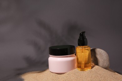 Cosmetic products and stone on sand against grey background. Space for text