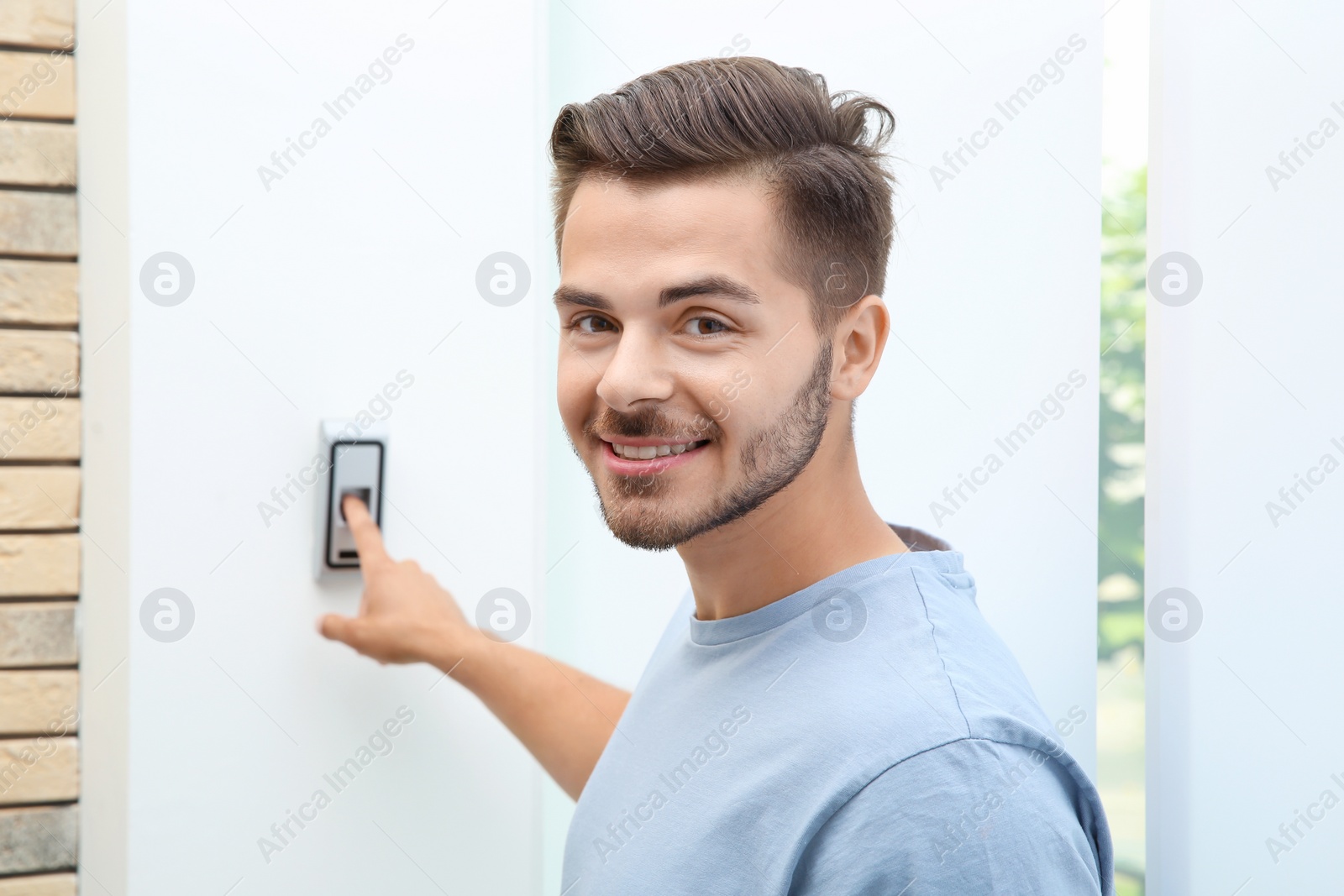 Photo of Young man pressing fingerprint scanner on alarm system indoors