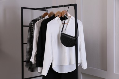 Rack with stylish women's clothes and bag near light wall