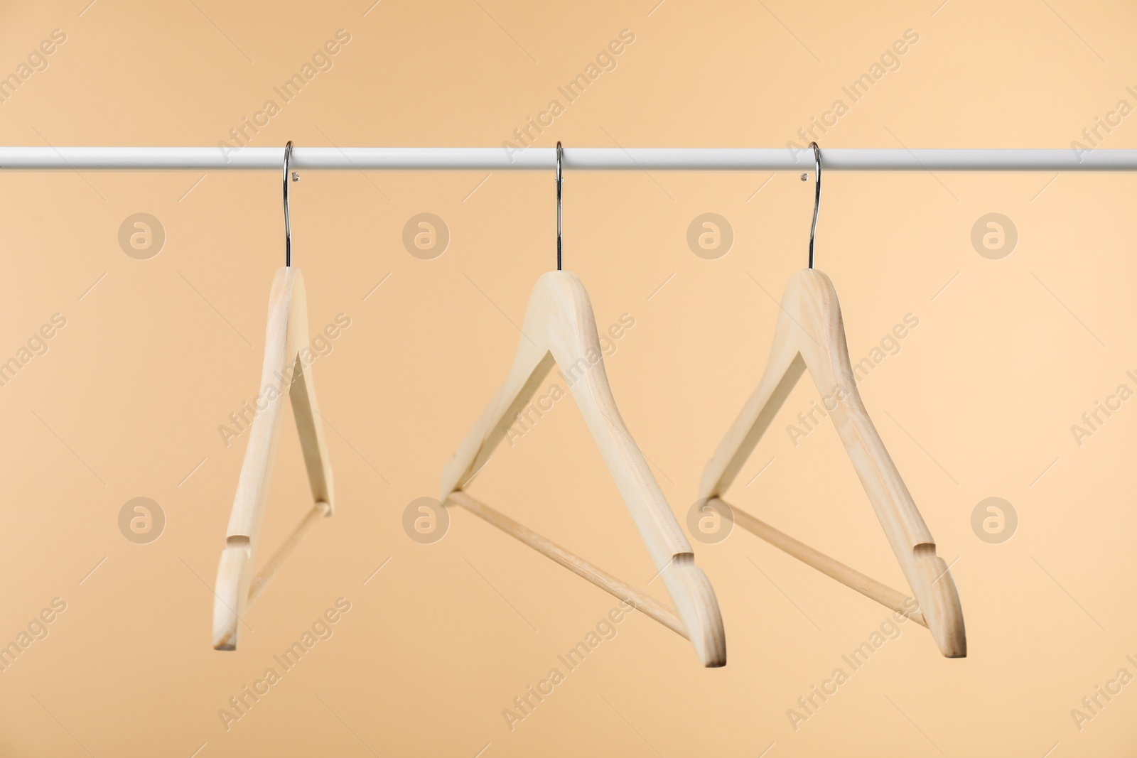 Photo of Empty clothes hangers on wooden rack against beige background