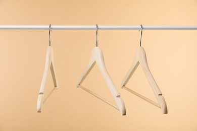 Photo of Empty clothes hangers on wooden rack against beige background