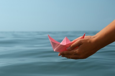 Photo of Woman holding pink paper boat near sea, closeup. Space for text