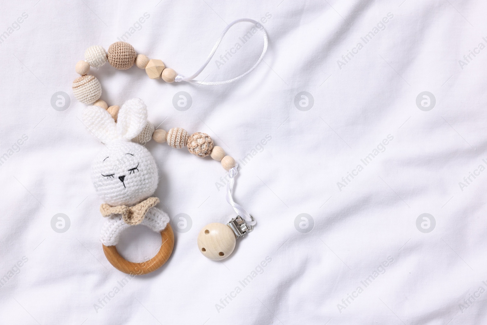 Photo of Baby accessories. Teether and pacifier clip on white fabric, top view. Space for text