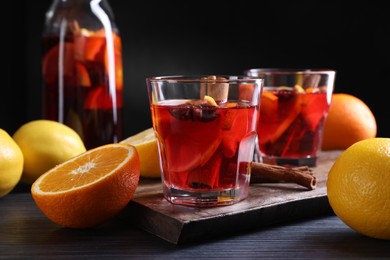 Photo of Aromatic punch drink and ingredients on black table, closeup