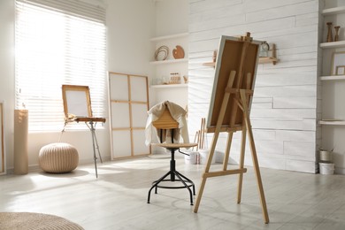 Photo of Modern studio interior with artist's workplace and foldable wooden easel near large window